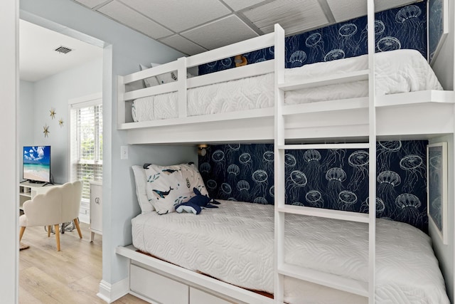 bedroom with a paneled ceiling, wood finished floors, and visible vents