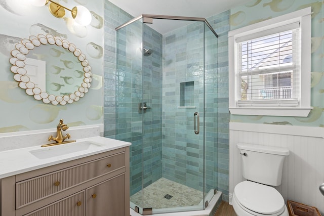 bathroom featuring toilet, a wainscoted wall, vanity, and a stall shower