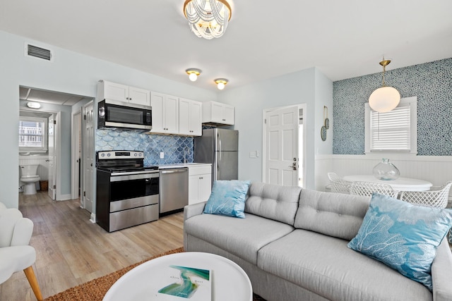 living room featuring a wainscoted wall, light wood-type flooring, visible vents, and wallpapered walls