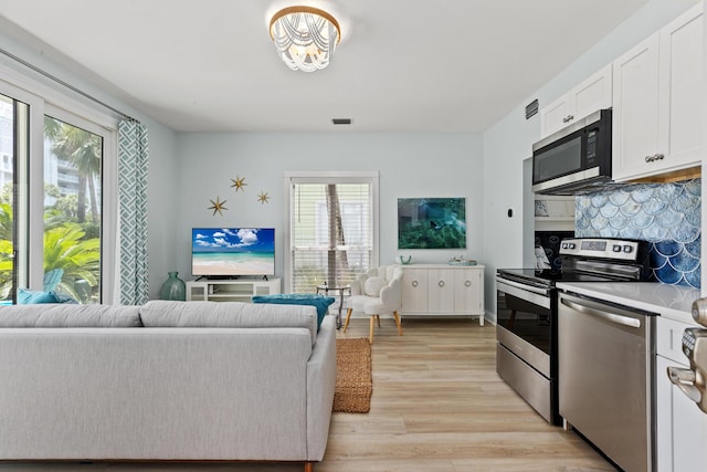 kitchen with stainless steel appliances, white cabinetry, open floor plan, light countertops, and light wood finished floors