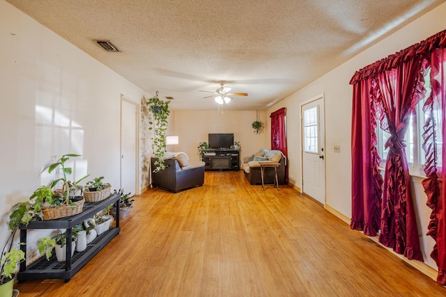 living room featuring ceiling fan, a textured ceiling, and light wood-type flooring