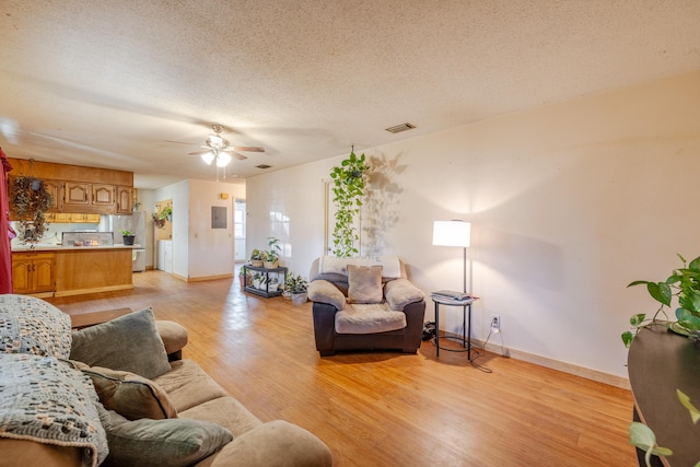 living room with ceiling fan, a textured ceiling, and light wood-type flooring