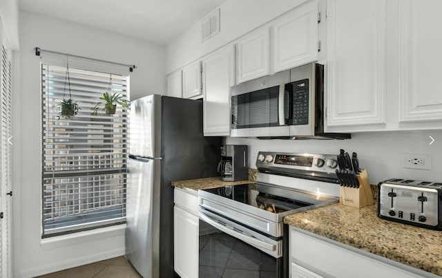 kitchen with appliances with stainless steel finishes, light tile patterned floors, white cabinets, and light stone counters