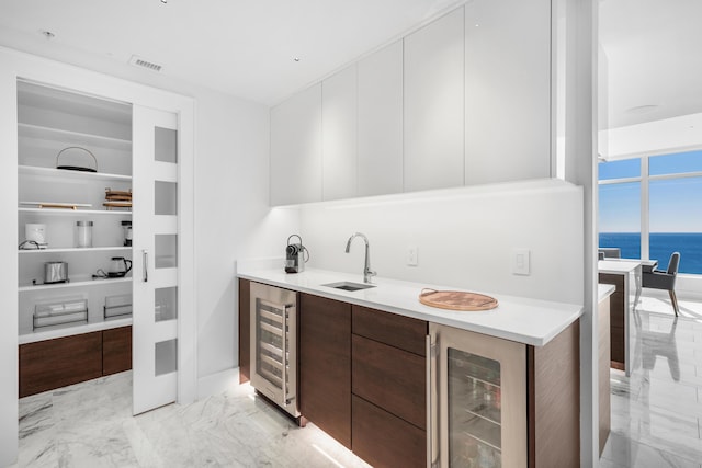 bar featuring beverage cooler, marble finish floor, a water view, and a sink