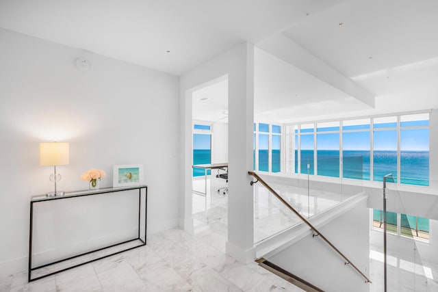 corridor with a water view, marble finish floor, baseboards, and an upstairs landing