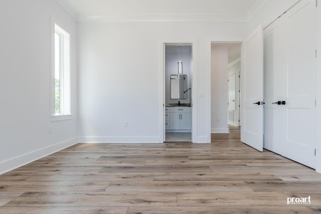 unfurnished bedroom featuring connected bathroom, ornamental molding, sink, and light wood-type flooring