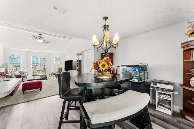 dining area featuring hardwood / wood-style flooring, vaulted ceiling, ceiling fan with notable chandelier, and a textured ceiling