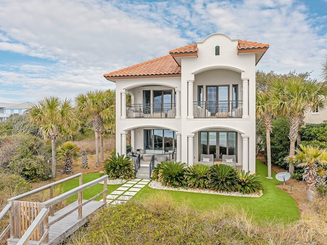 rear view of house with a balcony, stucco siding, french doors, a tile roof, and a lawn