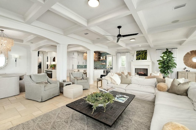 living area featuring ceiling fan, decorative columns, stone tile floors, arched walkways, and coffered ceiling