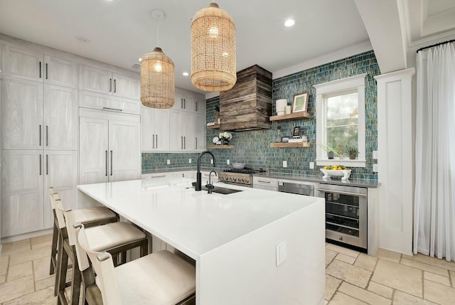 kitchen with stone tile floors, beverage cooler, premium range hood, recessed lighting, and a sink