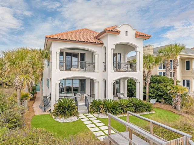 back of property featuring stucco siding, a tiled roof, a lawn, and a balcony