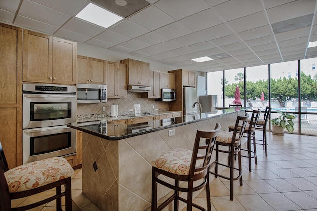 909 Santa Rosa Blvd Unit 611, Fort Walton Beach, FL 32548 - kitchen featuring stainless steel appliances, decorative backsplash, an island with sink, and dark stone countertops