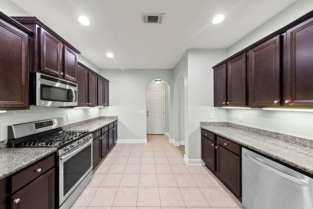 kitchen with light stone countertops, appliances with stainless steel finishes, dark brown cabinets, and light tile patterned flooring