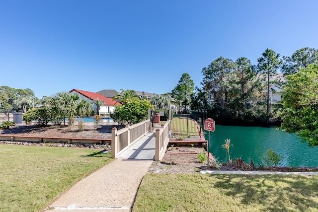 view of dock with a gate, a water view, a lawn, and fence