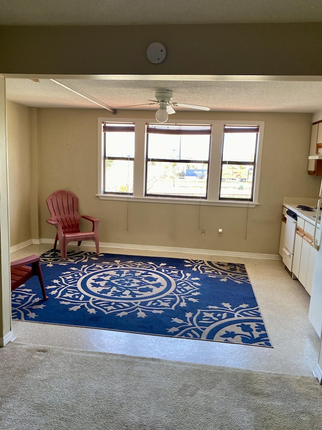 living area featuring a ceiling fan, light colored carpet, a healthy amount of sunlight, and baseboards