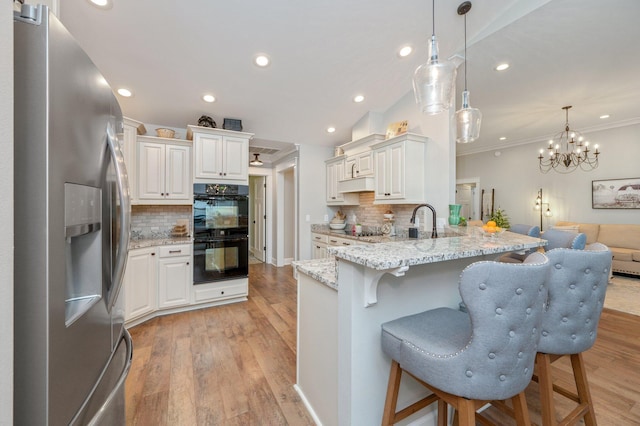 kitchen featuring pendant lighting, light stone counters, black appliances, white cabinets, and kitchen peninsula