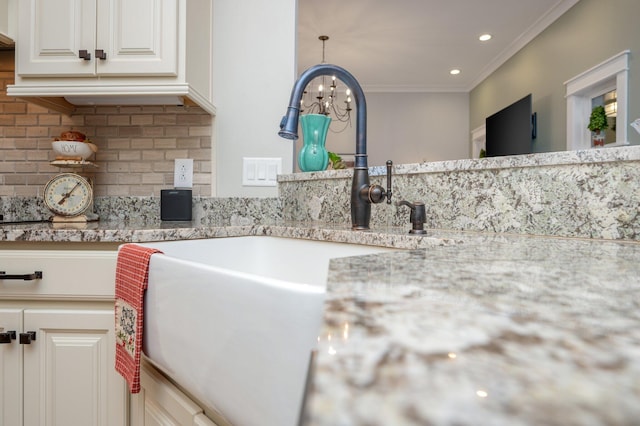 room details featuring crown molding, white cabinets, light stone counters, and backsplash