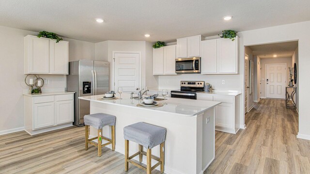 kitchen with an island with sink, appliances with stainless steel finishes, light countertops, a kitchen bar, and white cabinetry