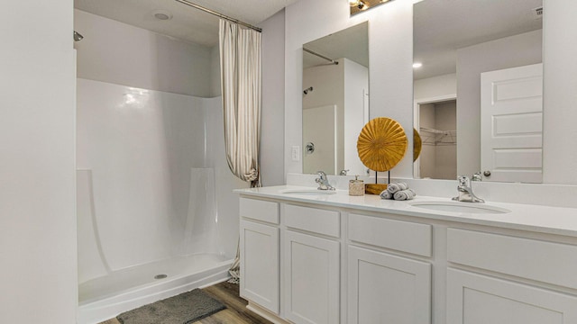 full bathroom with double vanity, wood finished floors, a sink, and a shower stall