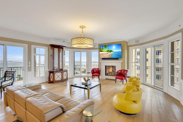 living room featuring light wood-type flooring, plenty of natural light, a water view, and ornamental molding