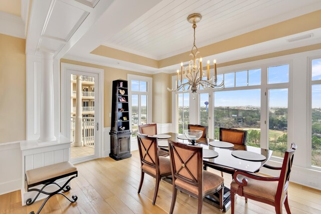 dining space with light hardwood / wood-style floors, ornamental molding, ornate columns, a raised ceiling, and a chandelier