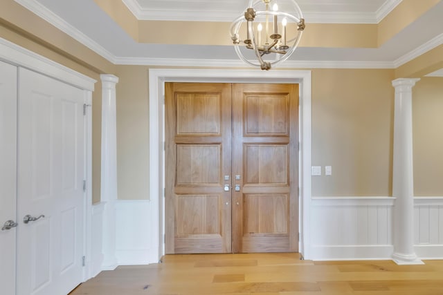 foyer entrance with light wood-type flooring, ornate columns, an inviting chandelier, and a raised ceiling