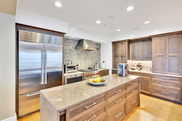 kitchen featuring light wood-type flooring, a kitchen island, light stone counters, wall chimney range hood, and premium appliances