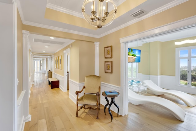 sitting room with a chandelier, a raised ceiling, crown molding, light wood-type flooring, and ornate columns