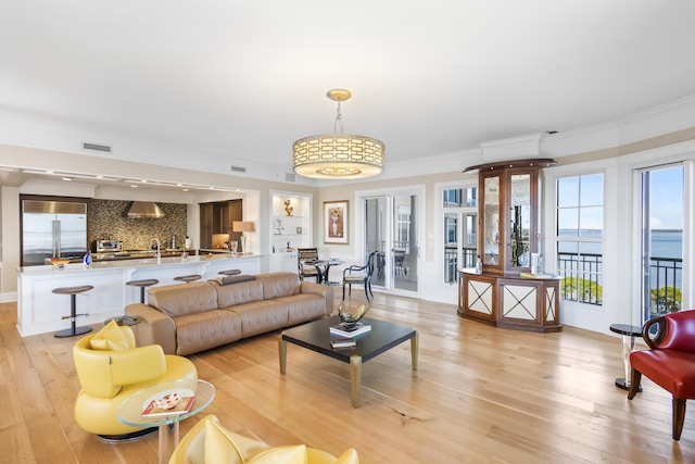 living room with light wood-type flooring, ornamental molding, sink, and a water view