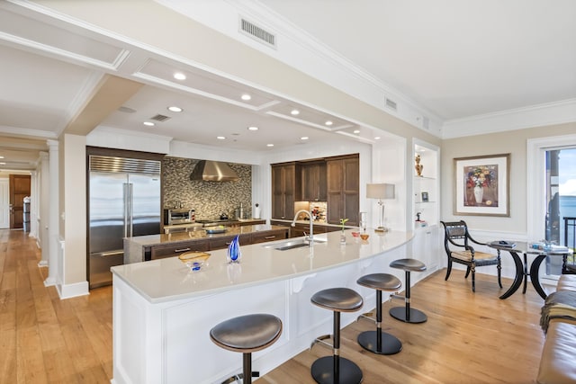 kitchen featuring stainless steel built in fridge, light hardwood / wood-style flooring, a kitchen breakfast bar, wall chimney exhaust hood, and sink