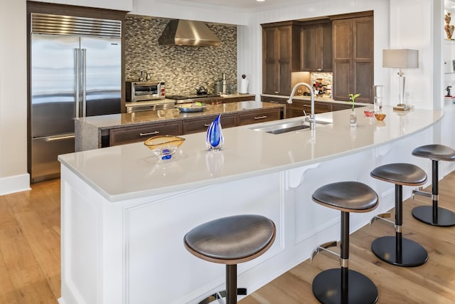 kitchen featuring light wood-type flooring, a spacious island, sink, appliances with stainless steel finishes, and wall chimney range hood