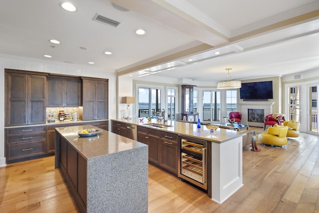 kitchen featuring an island with sink, light stone countertops, wine cooler, light hardwood / wood-style floors, and sink