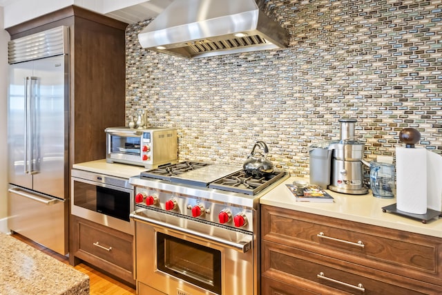 kitchen with light hardwood / wood-style flooring, high end appliances, wall chimney exhaust hood, light stone counters, and decorative backsplash