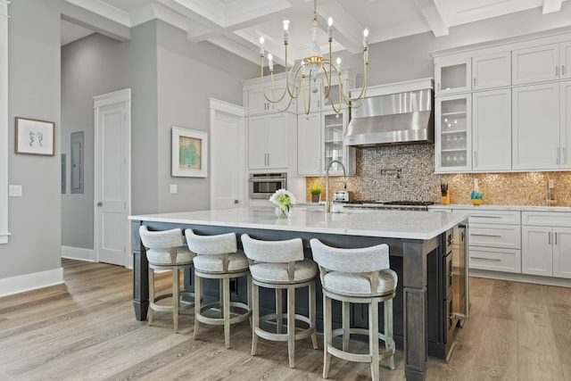 kitchen featuring a kitchen island with sink, white cabinets, wall chimney exhaust hood, and stainless steel oven