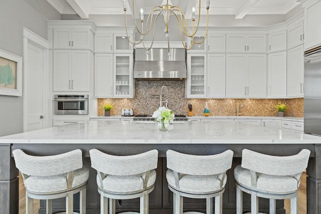 kitchen with wall chimney exhaust hood, a kitchen bar, decorative light fixtures, a large island with sink, and appliances with stainless steel finishes