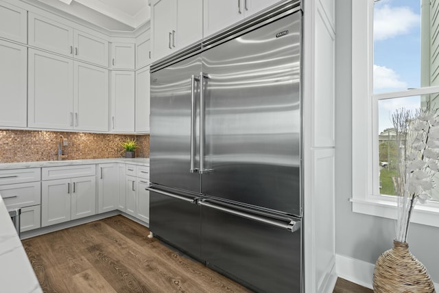 kitchen featuring dark hardwood / wood-style floors, tasteful backsplash, white cabinets, stainless steel built in fridge, and light stone counters