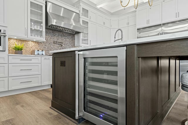 kitchen featuring wine cooler, white cabinetry, light hardwood / wood-style flooring, wall chimney range hood, and backsplash