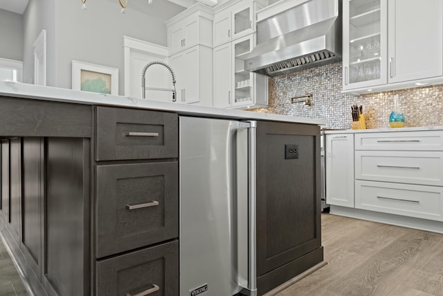 kitchen with white cabinetry, wall chimney exhaust hood, light wood-type flooring, and backsplash