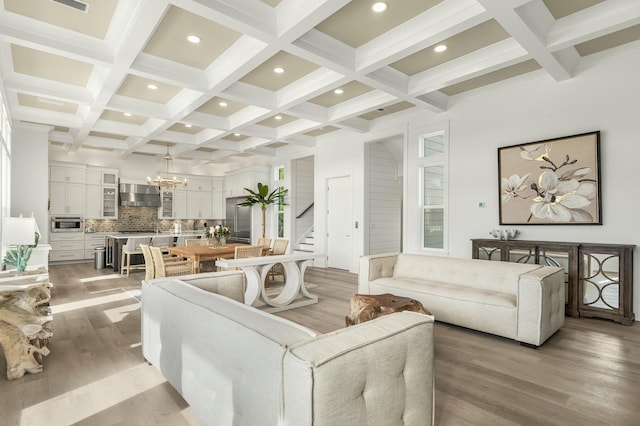 living room featuring coffered ceiling, beam ceiling, light hardwood / wood-style flooring, and a notable chandelier