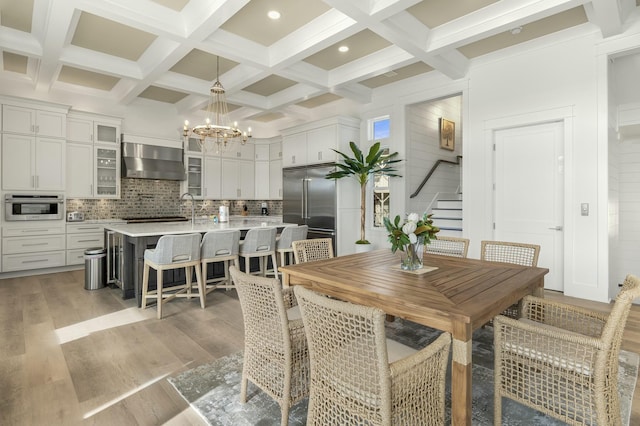 dining room featuring an inviting chandelier, beam ceiling, coffered ceiling, and light wood-type flooring