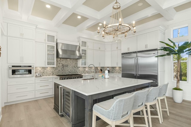 kitchen featuring stainless steel appliances, white cabinetry, a center island with sink, and wall chimney range hood