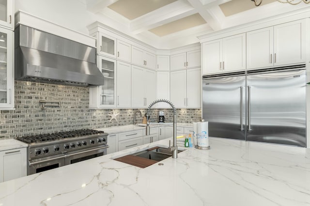 kitchen featuring wall chimney exhaust hood, high quality appliances, light stone counters, and white cabinets