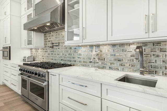 kitchen with sink, white cabinets, light stone counters, stainless steel appliances, and wall chimney exhaust hood