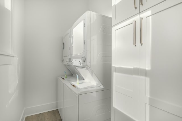 laundry area with stacked washer and dryer, hardwood / wood-style floors, and cabinets