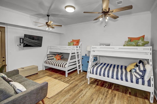 bedroom with a ceiling fan, visible vents, crown molding, and wood finished floors