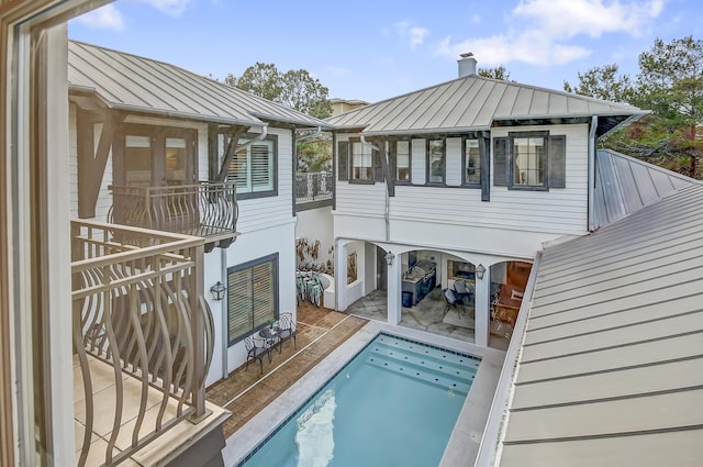 back of house featuring a standing seam roof, a swimming pool, metal roof, and a patio