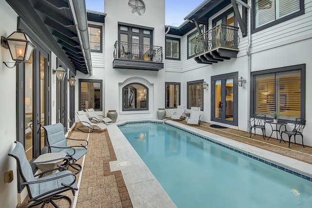 rear view of property with an outdoor pool, french doors, and stucco siding