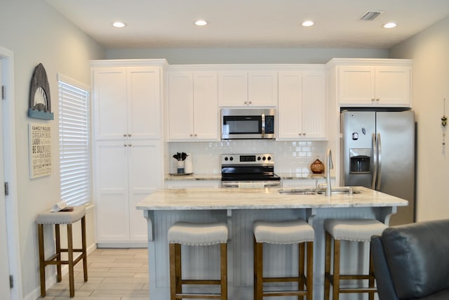 kitchen with sink, a breakfast bar area, appliances with stainless steel finishes, white cabinetry, and a center island with sink