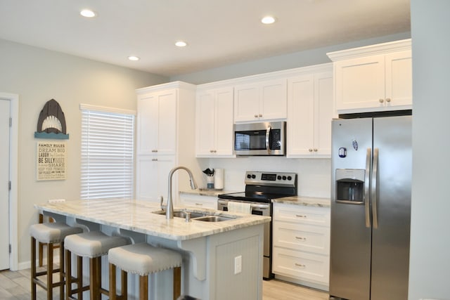 kitchen featuring sink, an island with sink, stainless steel appliances, light stone countertops, and white cabinets