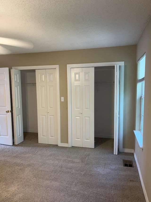 unfurnished bedroom featuring carpet, baseboards, visible vents, a textured ceiling, and two closets